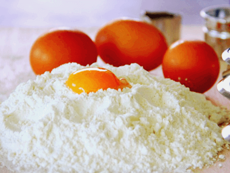 하얀색 밀가루가 가득하고 그 안에 노란 달걀 노른자가 있다. 주변에 갈색 달걀 3개가 있다.