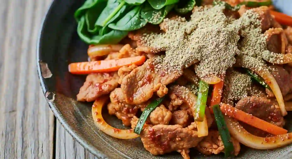 제육볶음에 시금치가 함께 들어 있고, 그 위에 들깨가 골고루 뿌려져 있는 모습.