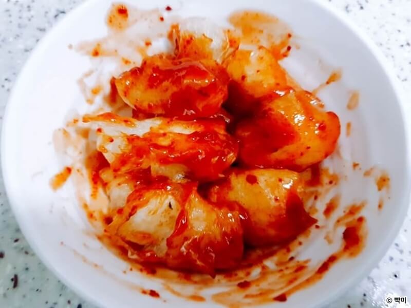 구운 닭강정을 양념치킨 소스에 골고루 버무리는 장면