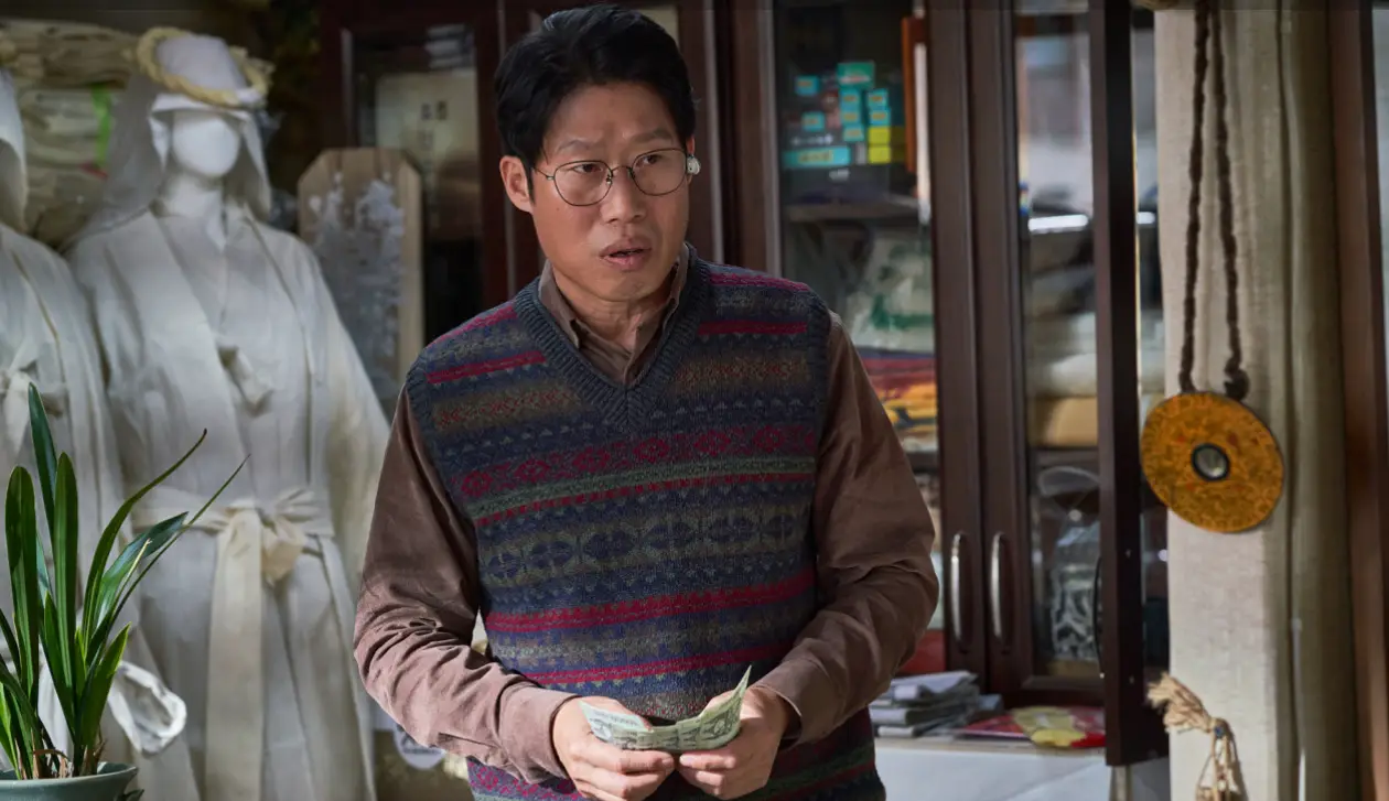 파묘- 흰 수의를 입은 마네킹이 있는 자신의 장의사가게에서 누군가와 얘기하고 있는 유해진