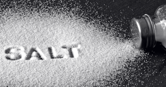 검정 식탁 위에 하얀 소금이 뿌려져 있고 오른 쪽에는 투명 유리병으로 된 소금병이 넘어져 있다.