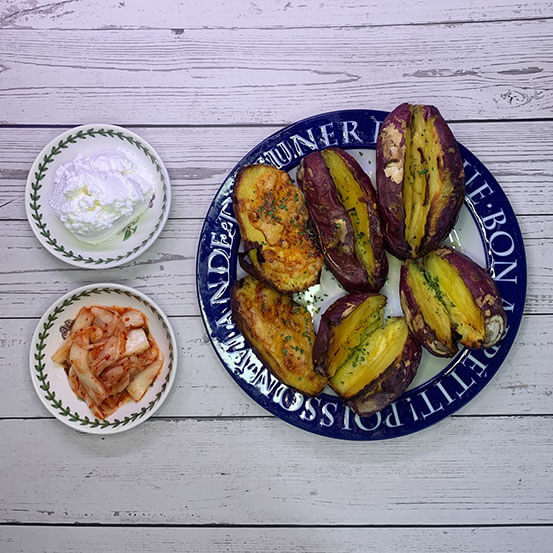 노릇노릇하고 먹음직스럽게 구워진 고구마 여섯 개가 파란색 테두리 접시에 담겨 있다. 소스용 그릇에 담긴 그릭요거트와 작은 종지에 담긴 김치가 함께 차려져 있다.