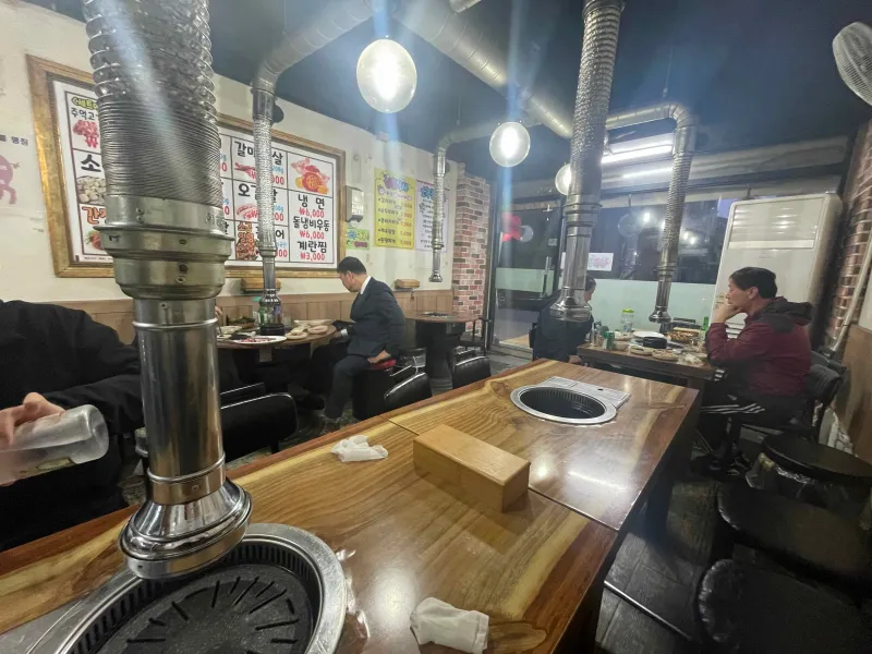 실내 테이블이 놓여져 있고 사람이 앉아있는 모습 연통이 테이블마다 놓여져 있다.