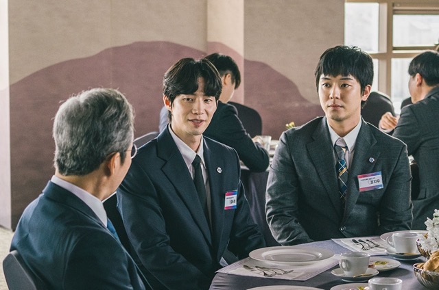 영화 《폭락》에서 암호화폐 기업의 신입 직원들이 투자자들과의 미팅 자리에 참석한 장면. 환한 웃음 뒤에는 불안과 긴장이 교차하며, 한순간의 선택이 인생을 바꿀 수 있다는 경고가 스며 있다.