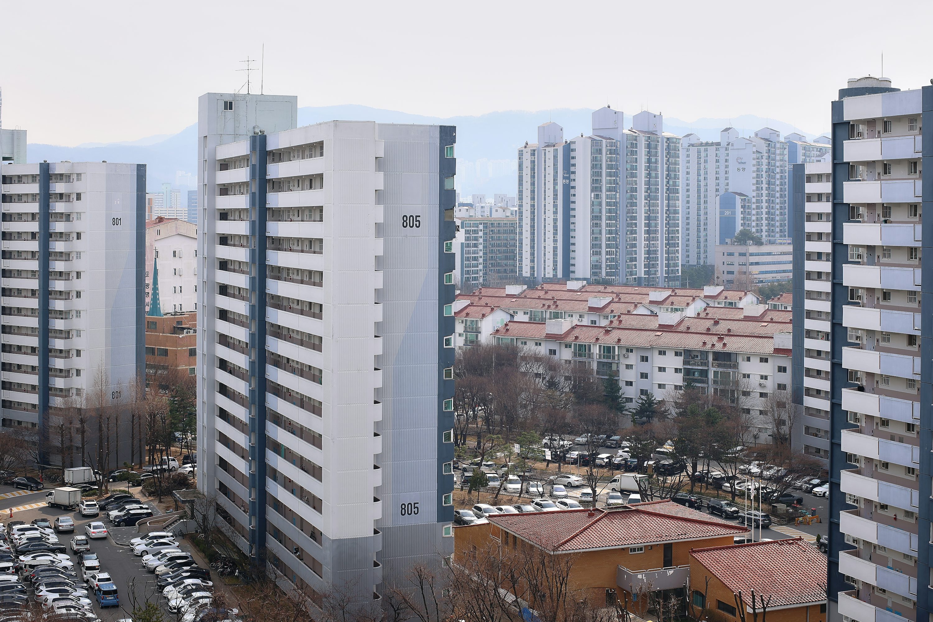고층 아파트 단지와 지상 주차장에 차들이 주차되어 있는 도심 풍경
