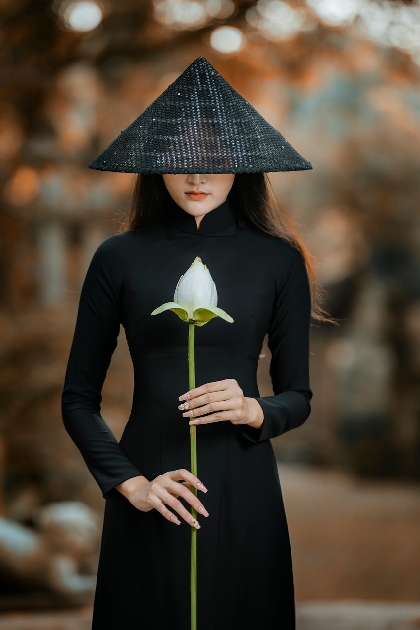 검은색 아오자이를 입고 검은색 베트남 전통 모자를 쓴 흰색 연꽃을 든 여인