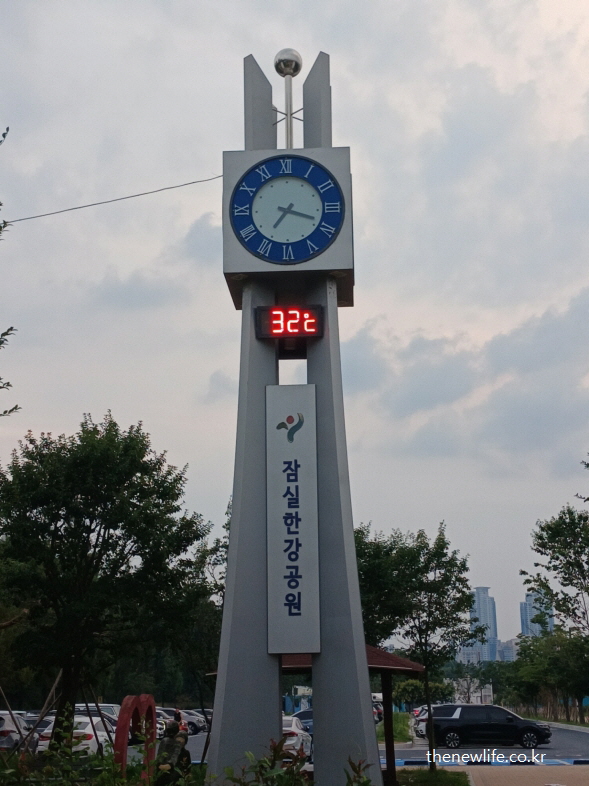 32도 온도를 표시하는 잠실한강공원 시계탑 – 무더운 날씨 속 물놀이장의 필요성을 보여주는 장면
