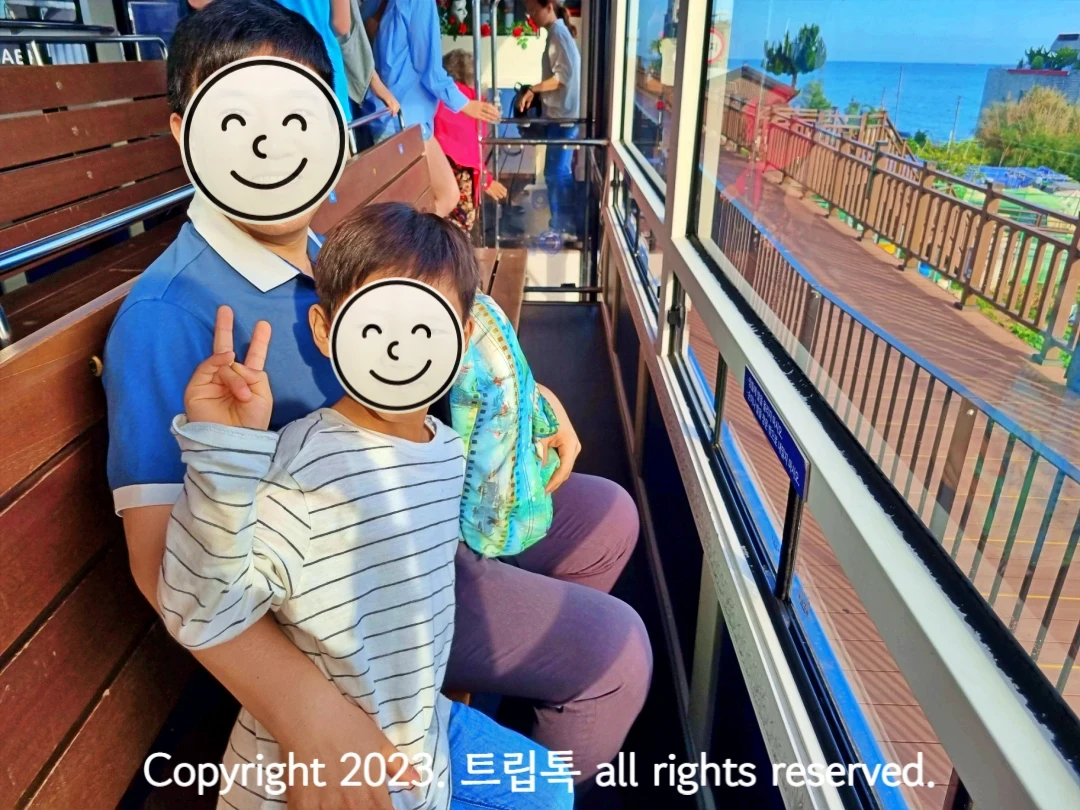 왼쪽에 나무로 되고 창문쪽을 바라본 의자에 앉은 두사람과 오른쪽의 열차 창밖에 보인다