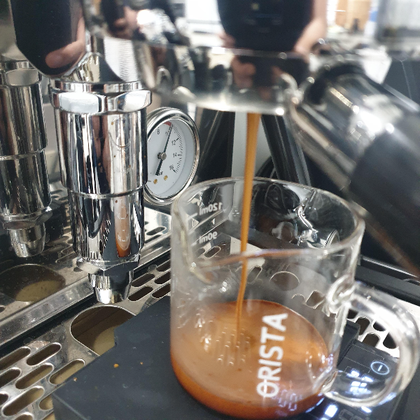 저울 위에 올려진 에스프레소 샷 잔에 추출되고 있는 에스프레소가 떨어지고 있다. 잔 속 크레마가 가득하다.