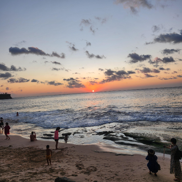 태양이 수평선에 걸려있다. 해변에서 노을을 보는 사람들