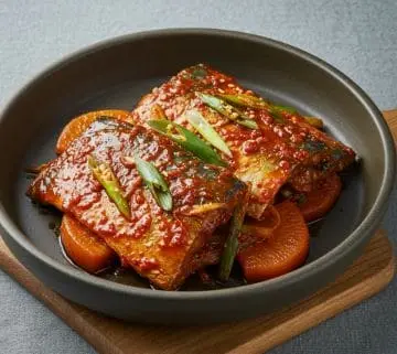 진한 양념과 대파가 올려진 고등어조림과 무가 검은 그릇에 담긴 모습
