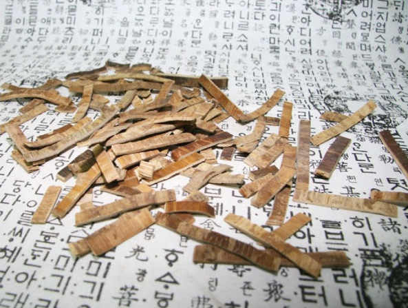 엄나무의 껍질(해동피)을 채취하여&#44; 잘 세척한 후&#44; 건조하여 일정 크기로 토막 내어 잘라서 옛날 글자가 새겨져 있는 종이 위에 흩어 놓은 사진