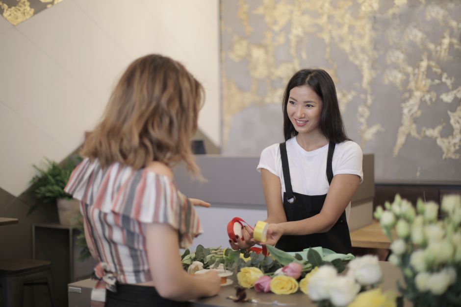 A smiling florist helps a customer with flower arrangements indoors.