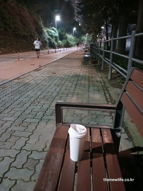 공원 벤치 위에 놓인 블랙커피 컵과 야간 조깅로의 풍경