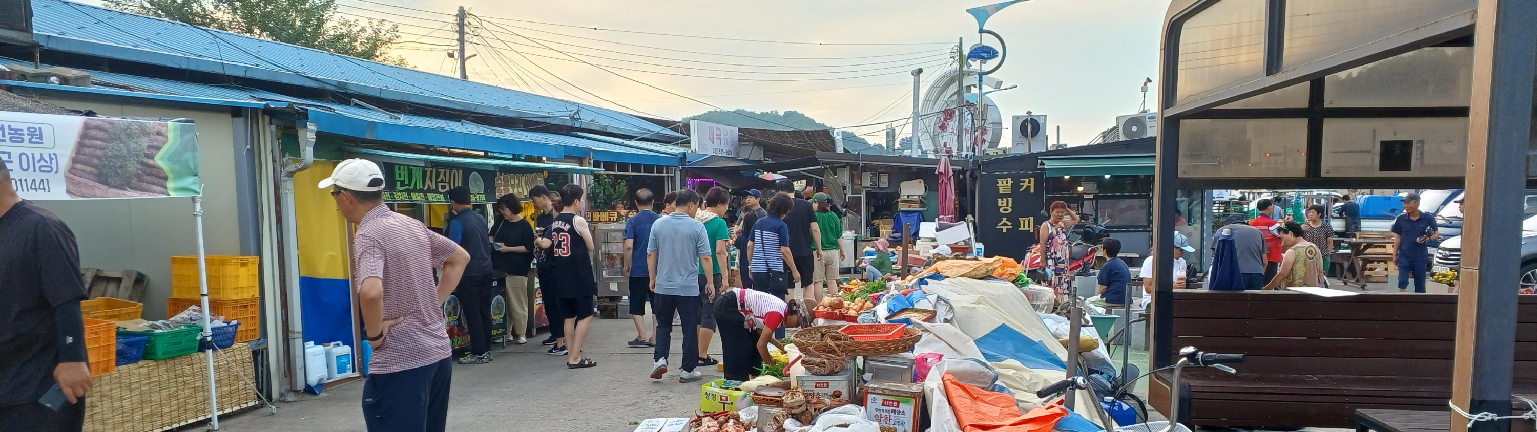 시장 통로를 따라 노점 좌판이 늘어서 있고, 방문객과 상인들이 오가며 장을 보는 새벽 시장 풍경