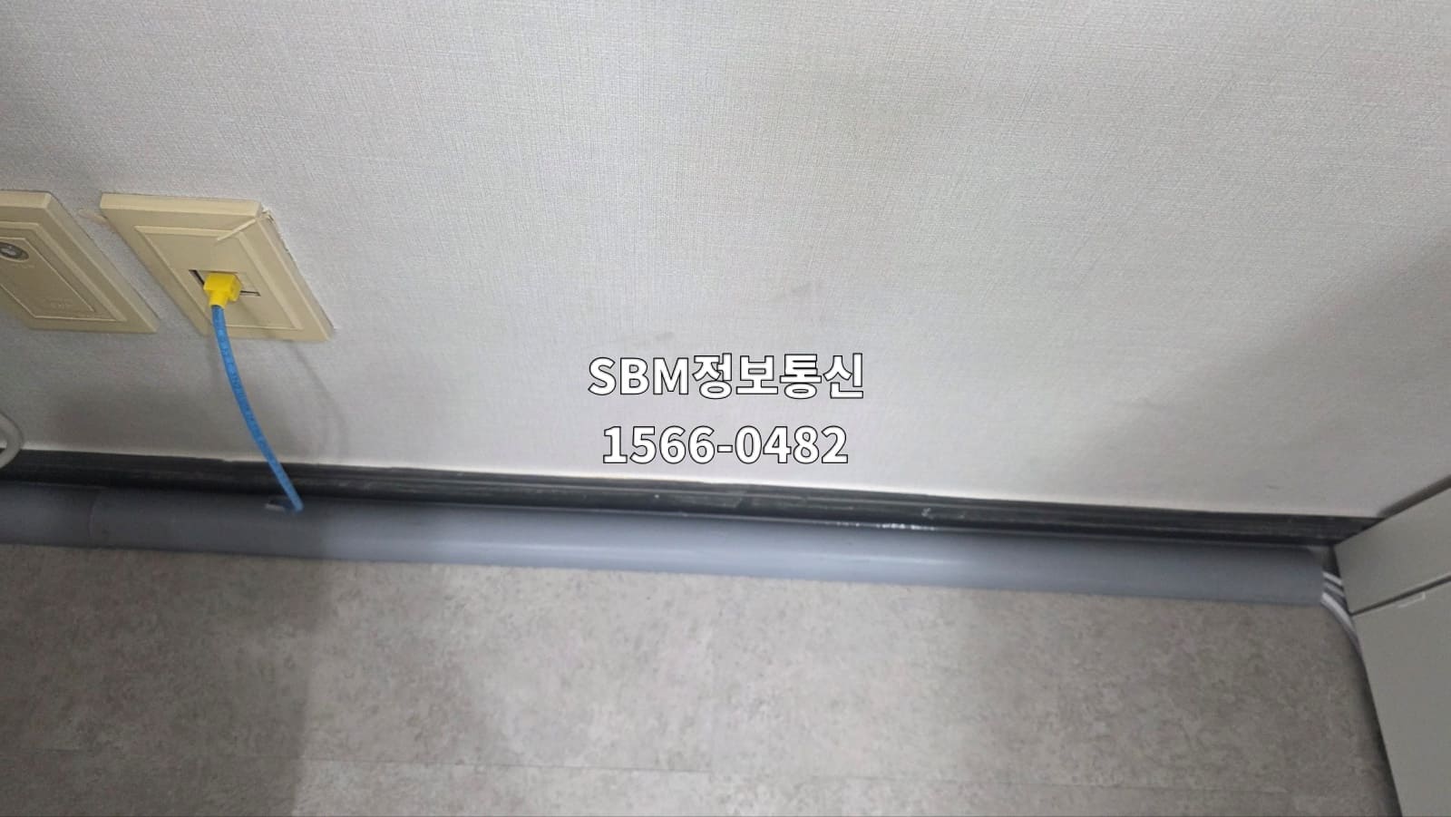 벽면 랜포트에서 나온 파란색 케이블을 검은색 걸레받이 라인에 맞춰 회색 몰딩으로 깔끔하게 정리한 모습