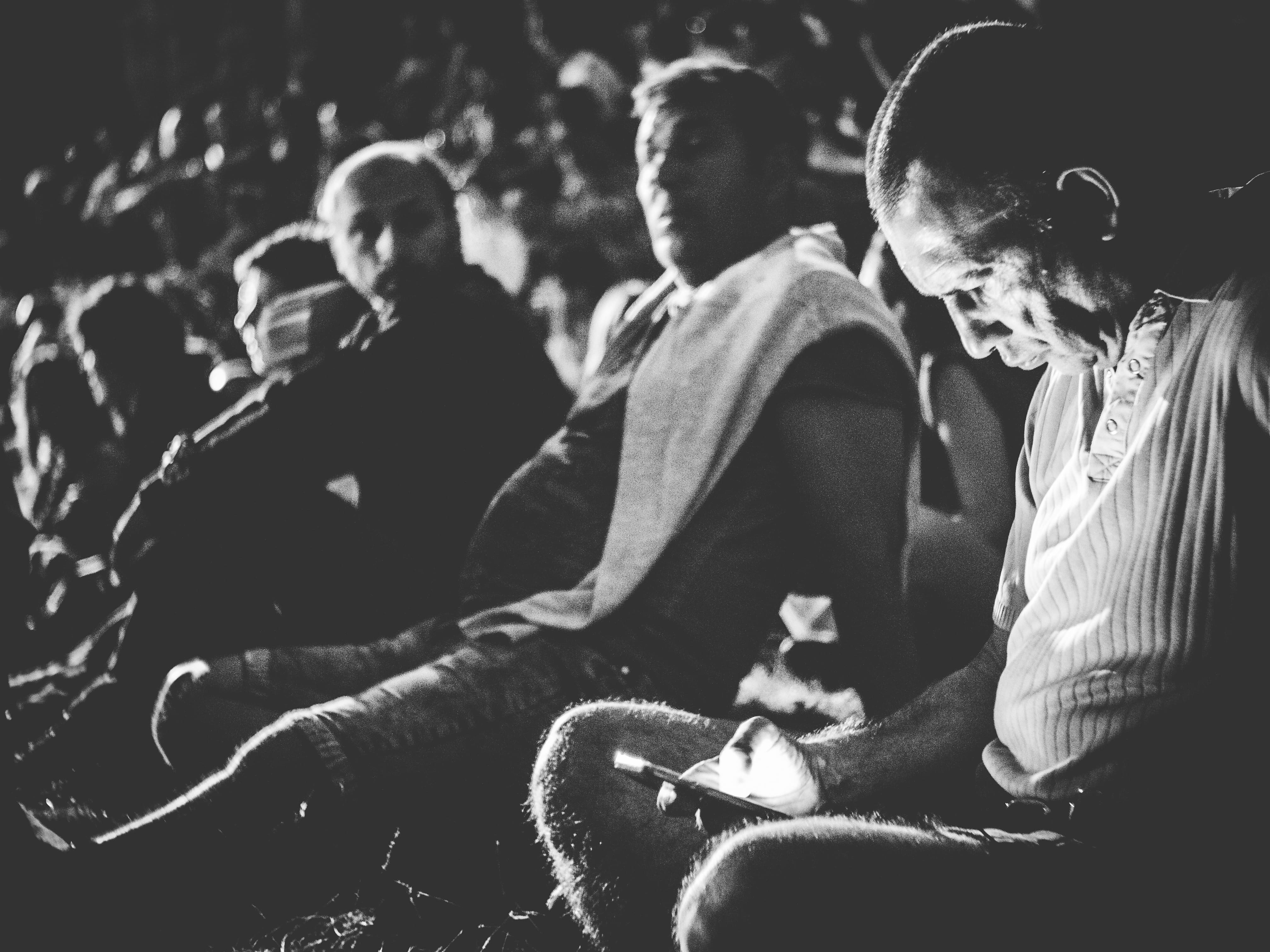 A man looking at his cell phone in a theater and men looking at him