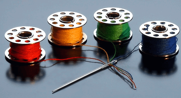 은색 바늘이 있다. 빨간색, 주황색 초록색, 남색 실이 있고 바늘 구멍에 실들이 들어갔다.