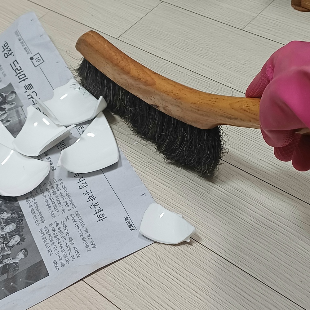 빗자루와 신문지를 이용해 깨진 도자기 조각을 정리하는 모습