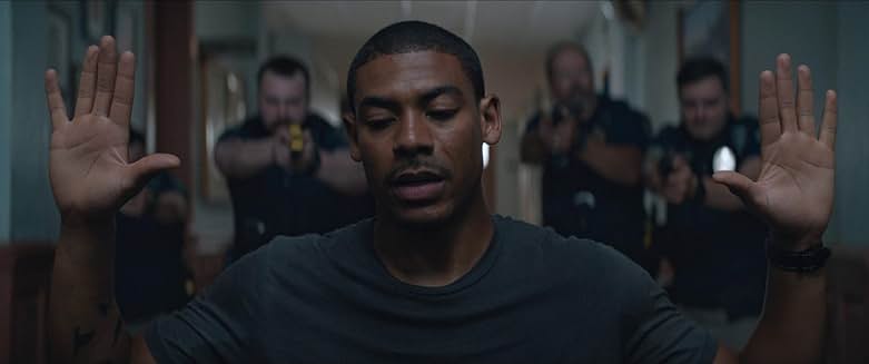 Rebel Ridge 영화 장면, 주인공이 손을 들고 경찰들에게 둘러싸인 장면