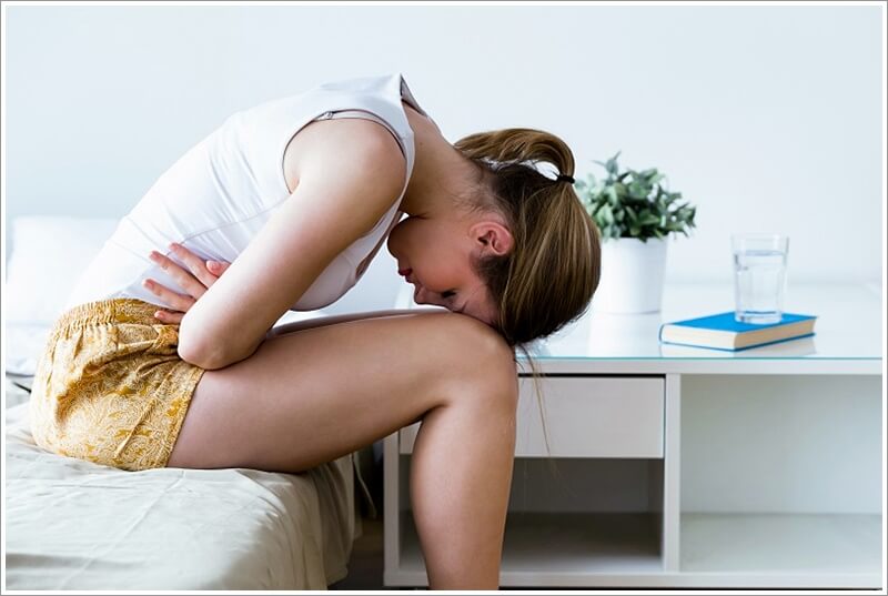 배탈 때문에 침대에서 앉아서 배를 부여 잡고 복통을 호소하고 있는 여성