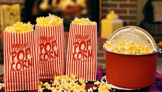 빨간 줄이 세로로 그어진 종이봉투 3개에 팝콘이 가득하고, 오른쪽에는 빨간 냄비에 팝콘이 가득하다.