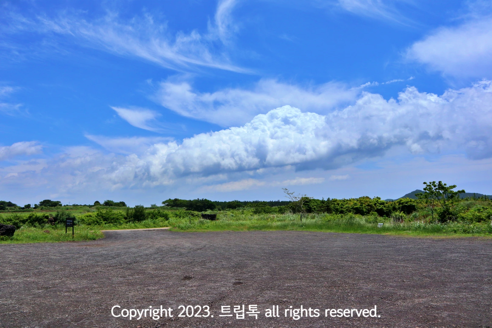 가운에 하얀 뭉게 구름이 있고 아래 검정색 돌이 깔린 평지이다.