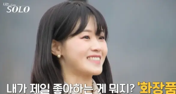 자연배경 검은리본이 달린 베이지색 원피스 긴웨이브머리를 하고 말하는 현숙의 옆모습 아래 흰글씨 내가 제일 좋아하는 게 뭐지? 화장품