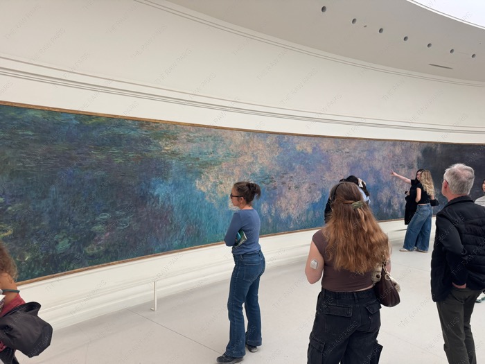 Visitors standing close to inspect details of Monet Water Lilies painting in Musée de l'Orangerie.