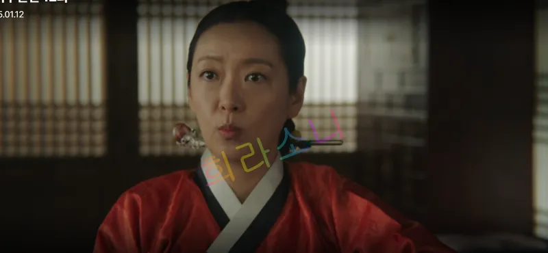 붉은 한복을 입은 홍씨부인이 입을 오무리며 의뭉스러운 표정을 짓고 있다.