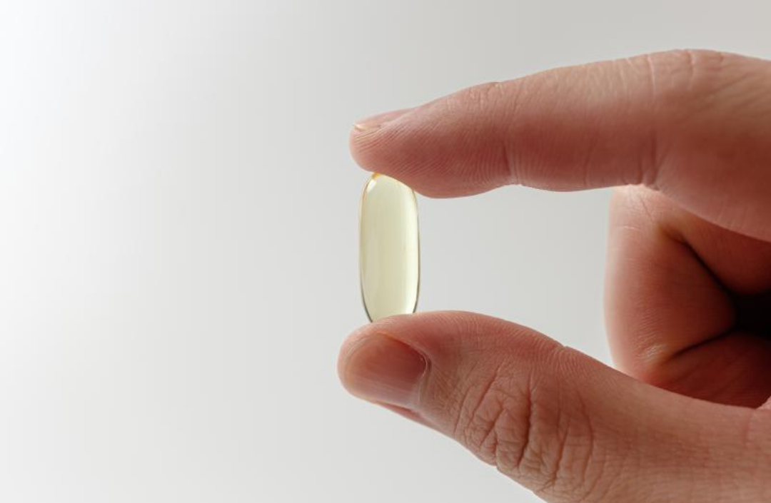 노란색의 연질 캡슐 한개를 들고 있다.
