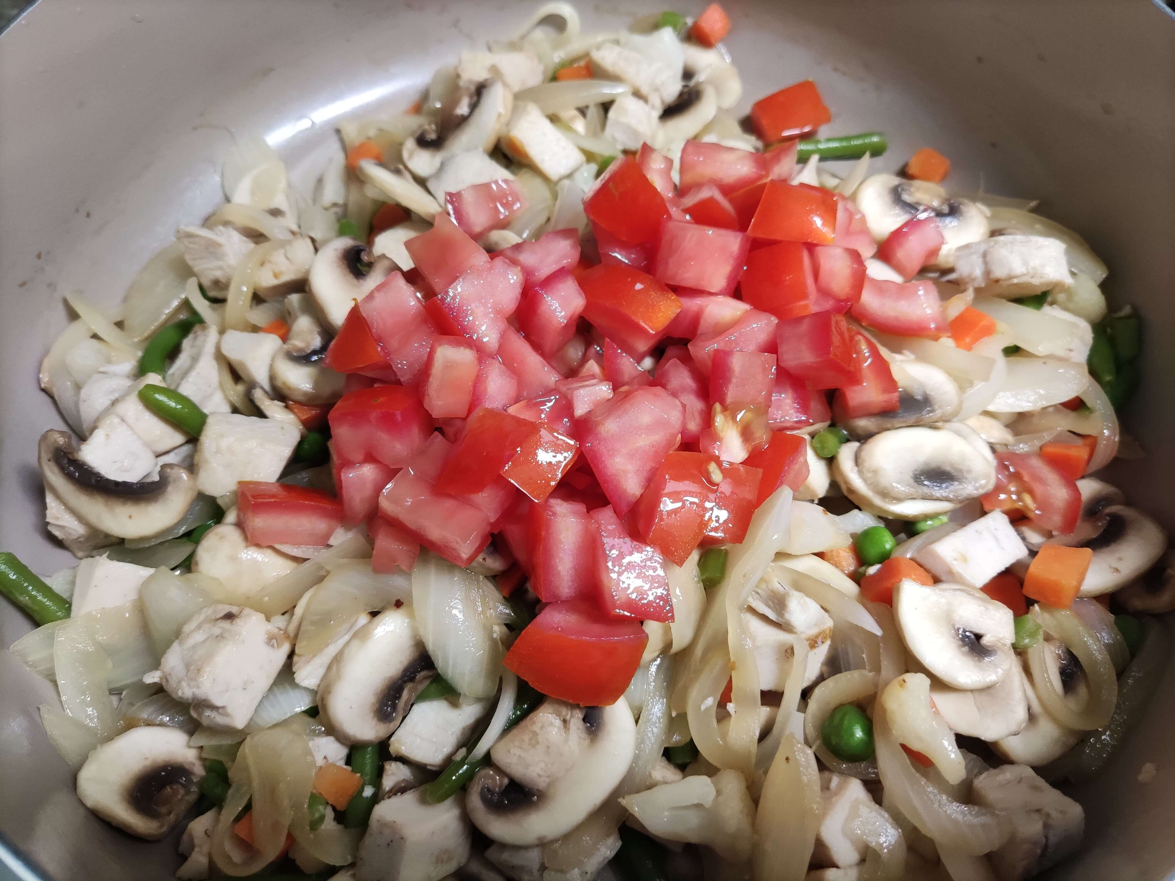 볶아진 재료들 위에 잘게 썬 토마토를 넣고 볶는 모습