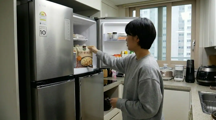 부엌 냉장고에서 냉동 볶음밥 봉지를 꺼내고 있는 여성