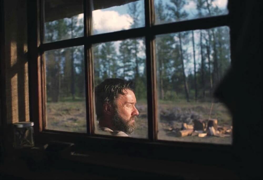 영화 기차의 꿈 스틸컷 – 오두막 창문 너머 사색에 잠긴 로버트