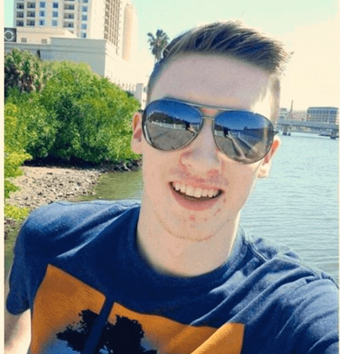 파란 여름 티셔츠를 입고 웃고있는 셰인 미슬러가 호숫가에서 셀카를 찍은 모습이다.