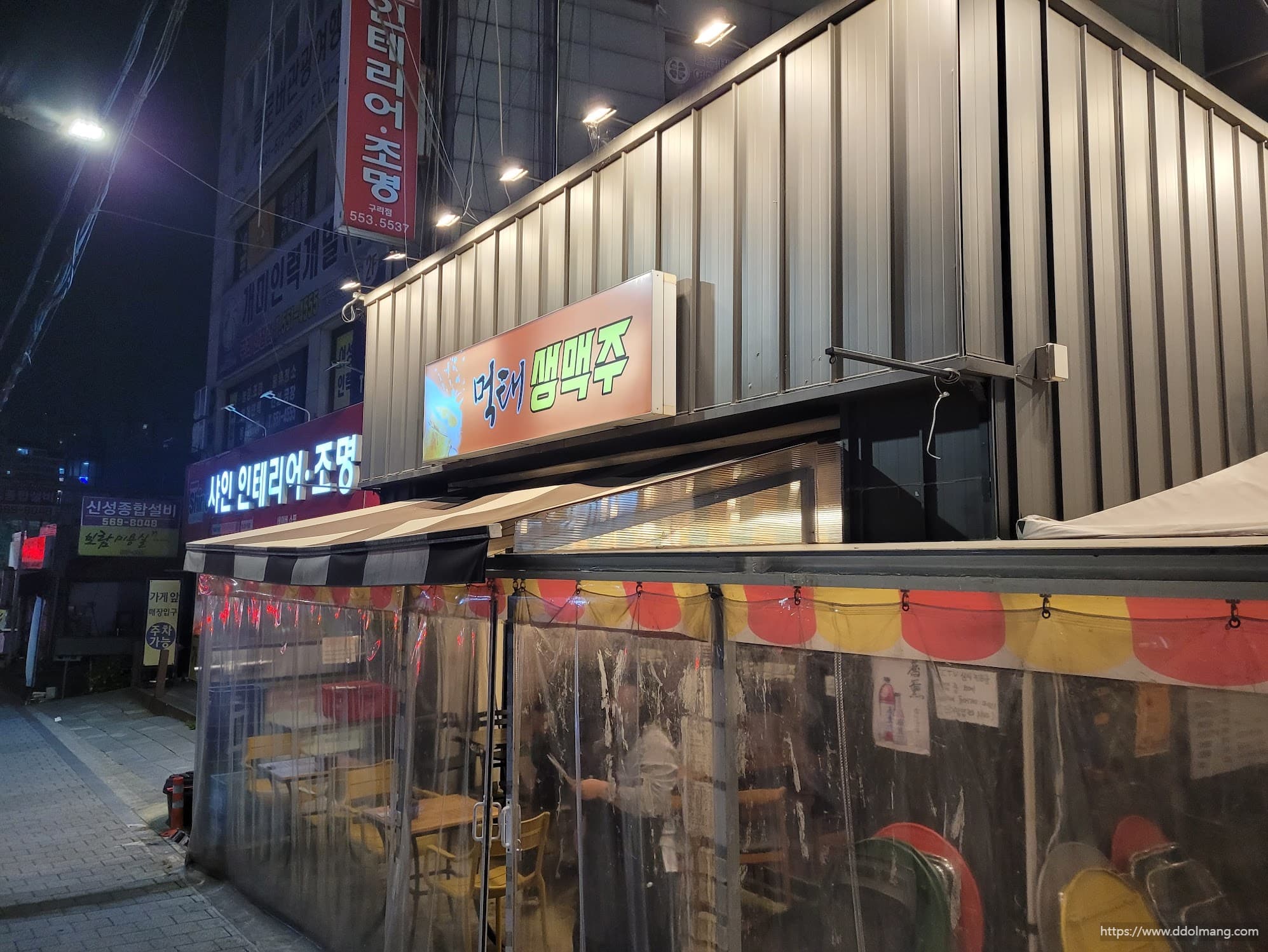 저녁시간 쯤 먹태생맥주 간판과 조명이 비친 가게 입구가 보이는 장면