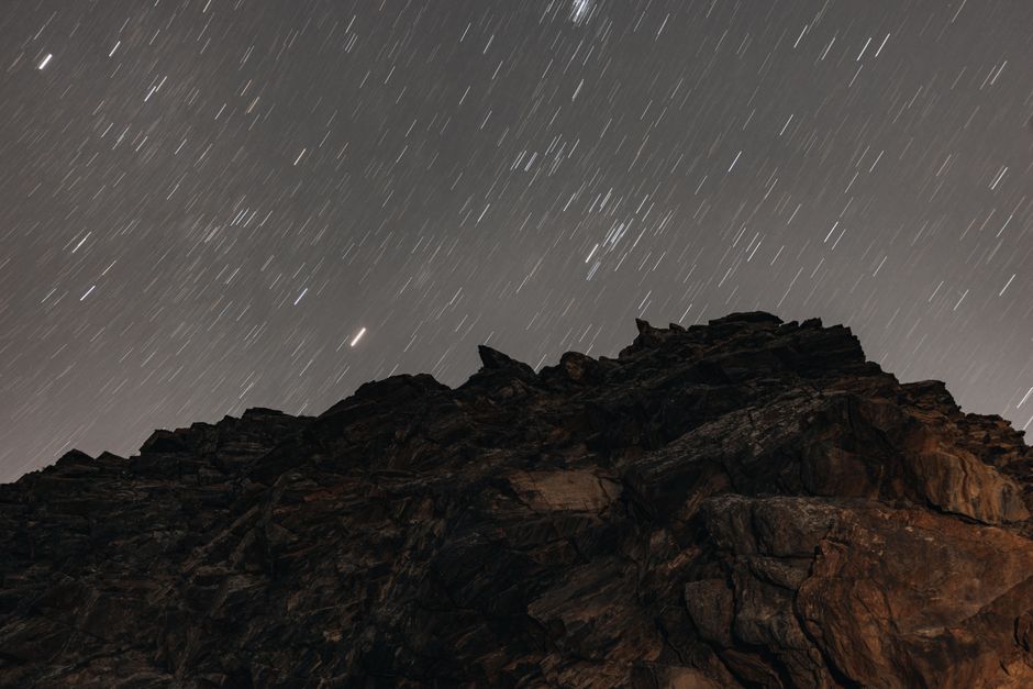 Long exposure capturing star trails over a rugged mountain peak at night.