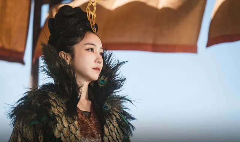 야외를 배경으로 공작털로 장식된 드레스와 금장식을 머리에 꼽고 있는 드라마 아라문의 검 태알하 캐릭터