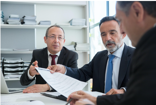 정장 차림의 전문가들이 사무실에서 문서를 검토하며 상담하는 모습