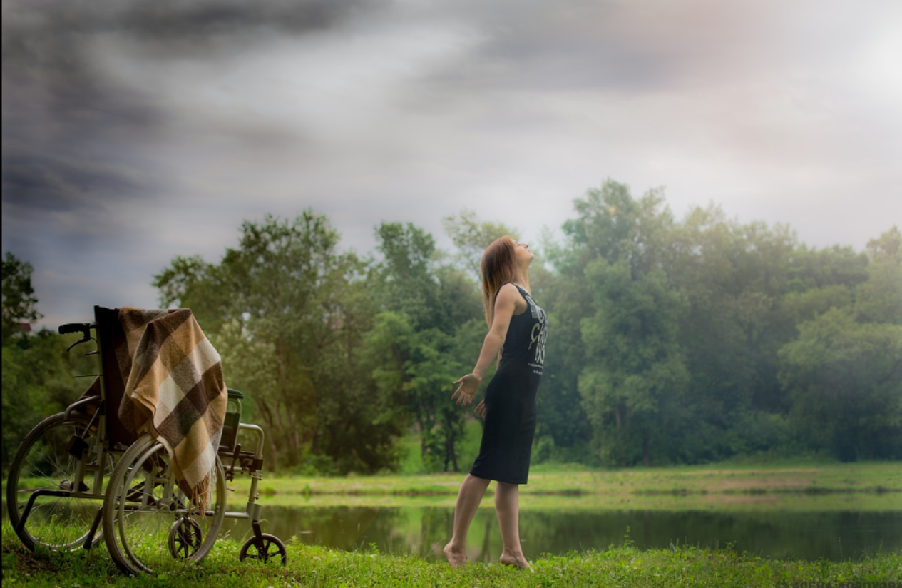 숲속에서 휠체어에서 일어나 기지개를 펴고 있는 여자 사진