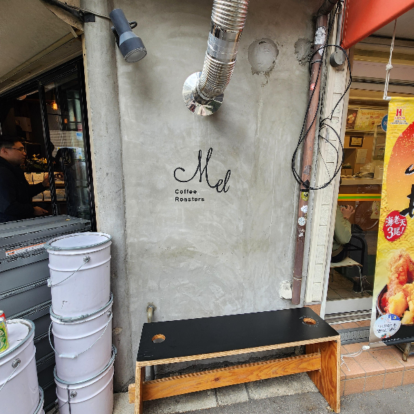 회색 벽면 Mel 로고가 있다. 그 아래 의자가 놓여 있다.