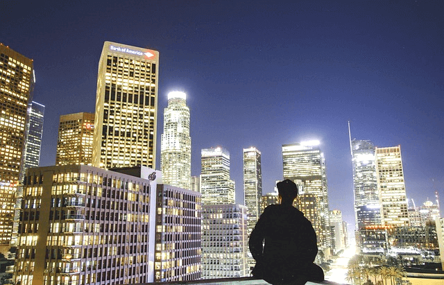 화려한 불빛이 반짝거리는 빌딩들이 모여있다. 그 앞에 젊은 남자가 빌딩을 바라보는 검정 실루엣이 그려졌다.