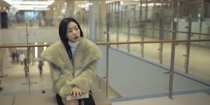 어느 대형 병원 2층 로비 벤치에 긴 생머리에 두툼한 베이지색 털 자켓을 걸치고 있는 드라마 유괴의 날의 서혜은을 연기하는 김신록 등장 장면