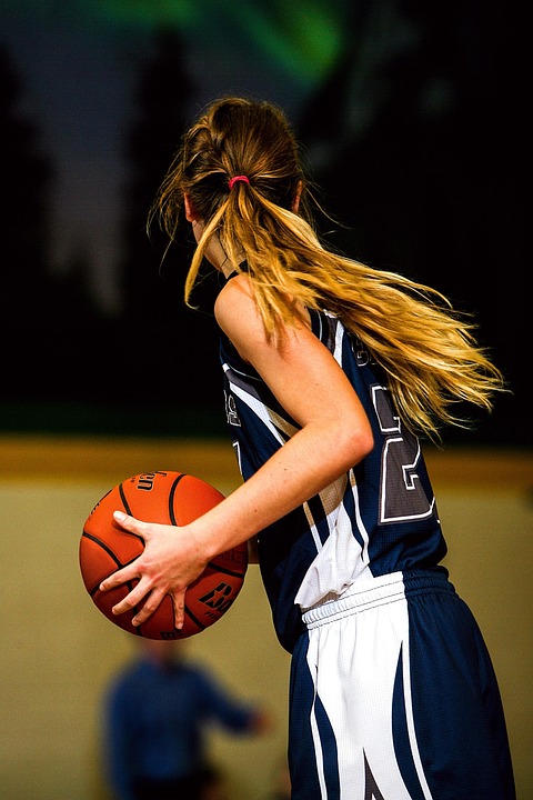 Young female basketball athlete dribbling and scanning court during high school or college level match