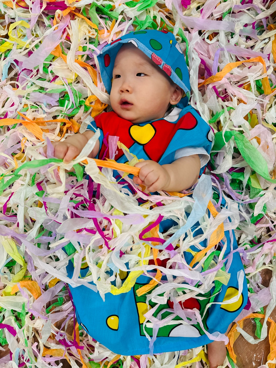 파란색 도트 의상을 입고 습자지 더미 위에 누워 놀고 있는 9개월 아기