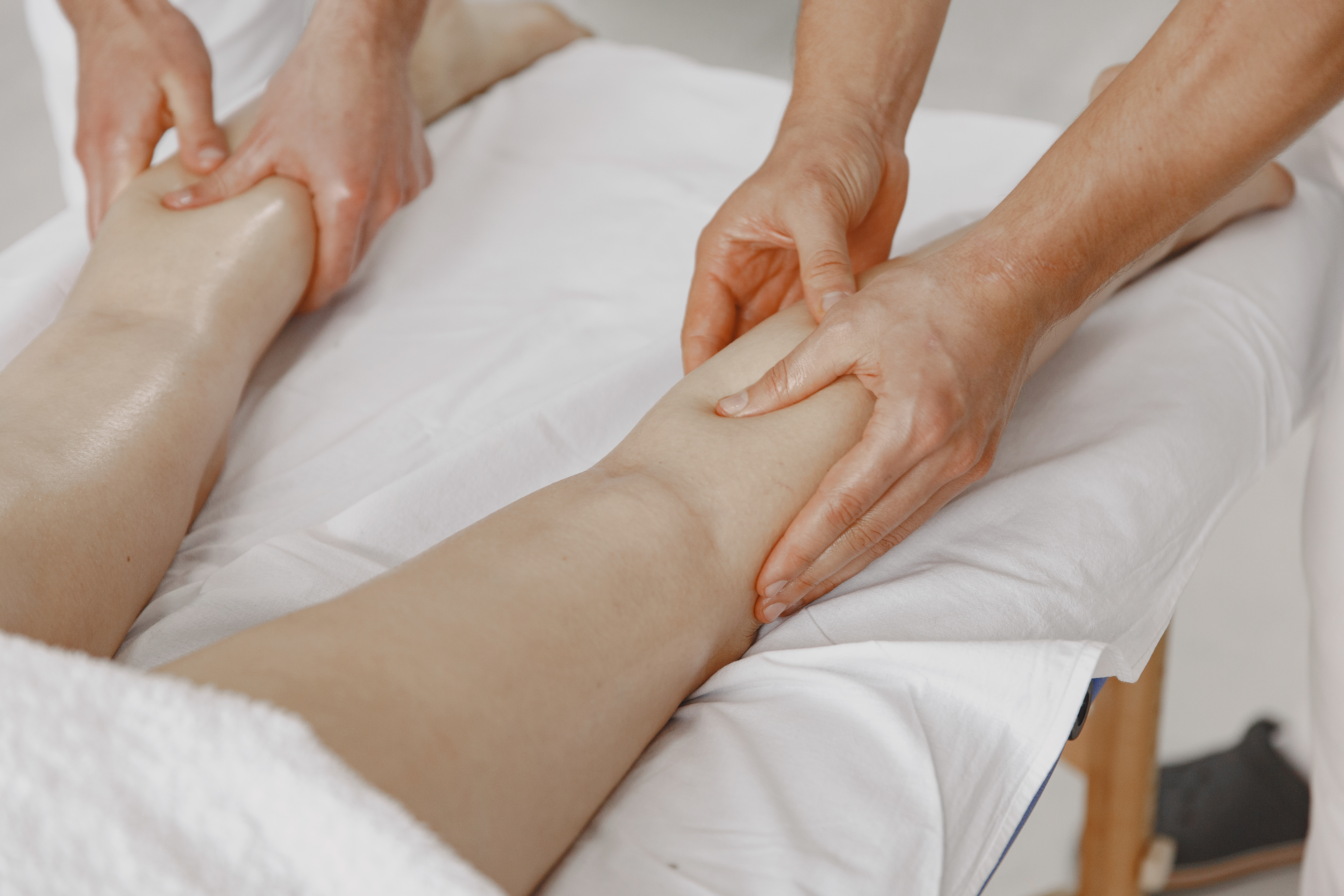 맛사지 관리실에서 2명의 맛사지사가 엎드려 있는 사람의 종아리를 한쪽씩 맡아서 종아리 근육을 풀고 있는 사진