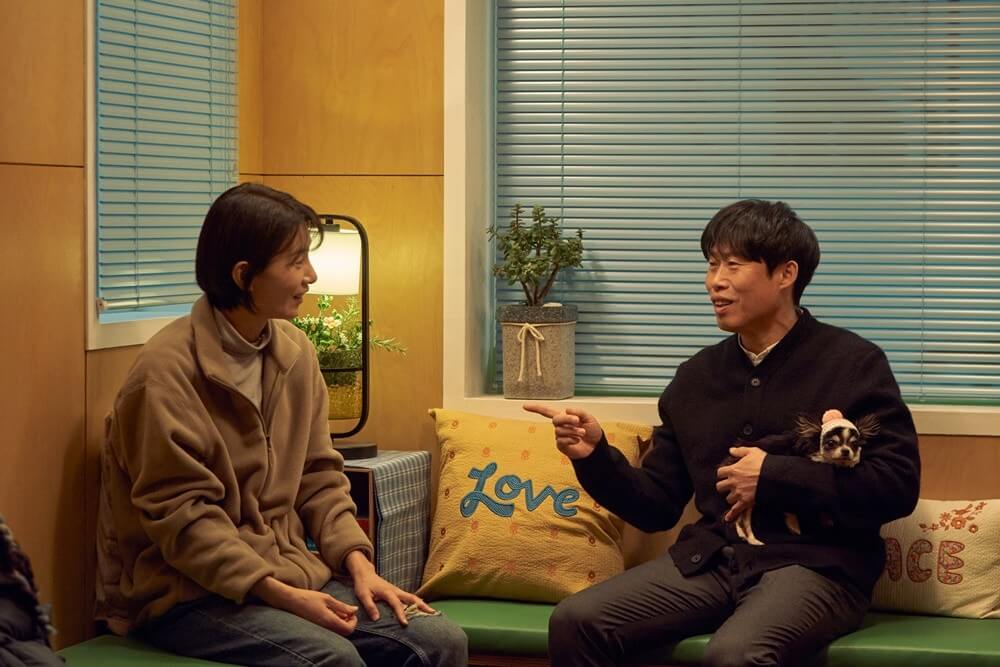 유해진 배우가 강아지를 안고 이야기하며 웃으며 김서형 배우를 손으로 가리키는 장면
