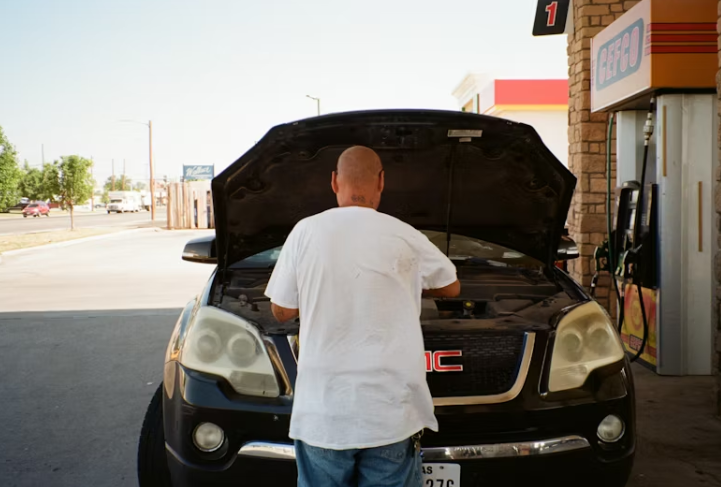 주유소 앞에서 차량 보닛을 열고 스스로 점검 중인 남성의 뒷모습