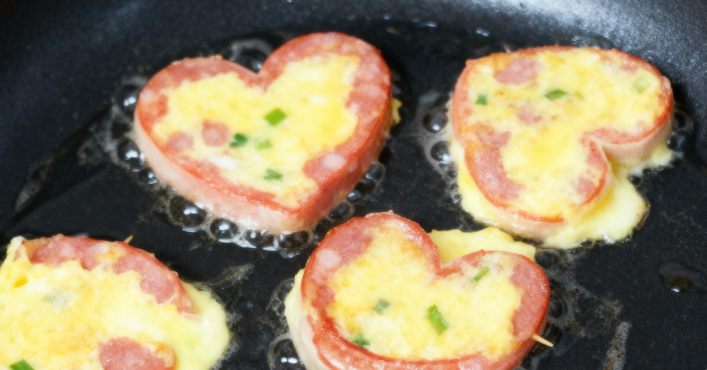 하트 모양 맛살 속에 노란 달걀물을 조심스레 채워 넣으며 지글지글 익히는 모습.