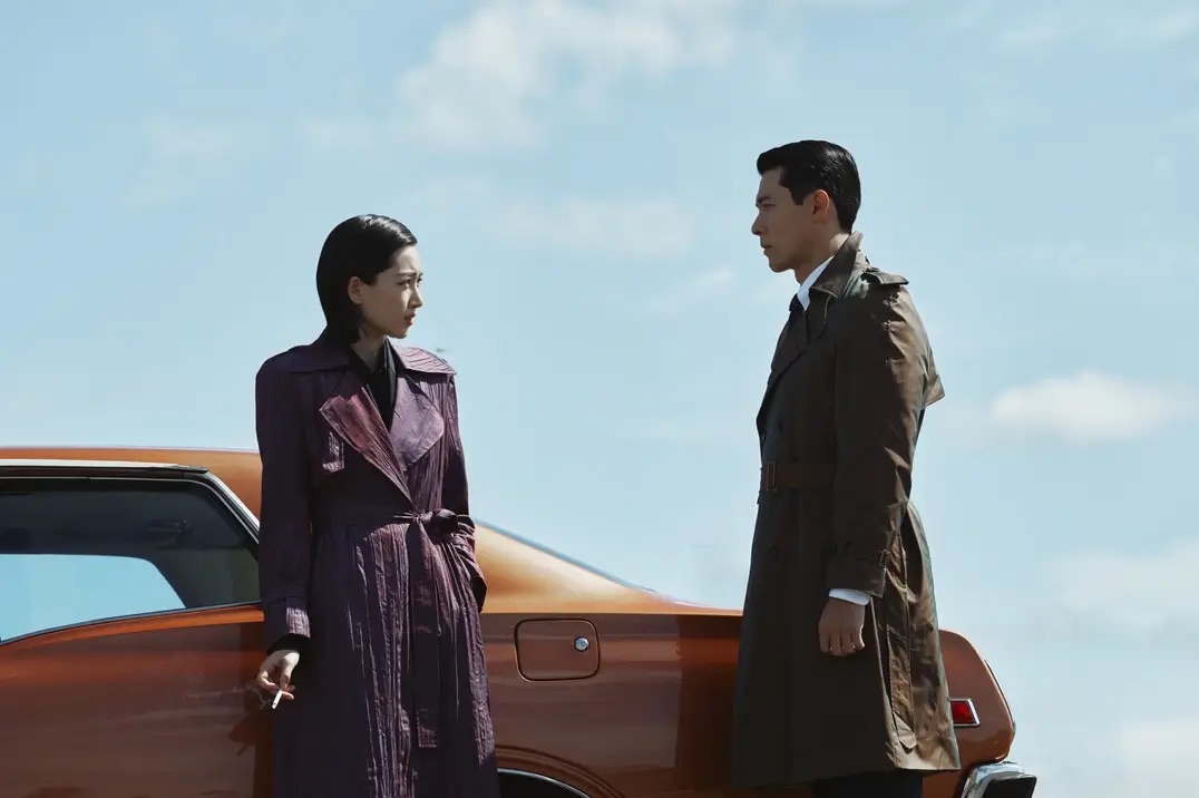 자동차 옆에 담배를 들고 있는 여자와 그 여자를 정면으로 쳐다보는 남자